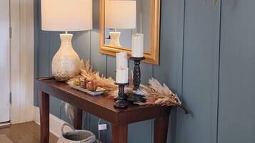 A wooden console table with two lamps, a mirror, and decorative items against a blue wall.