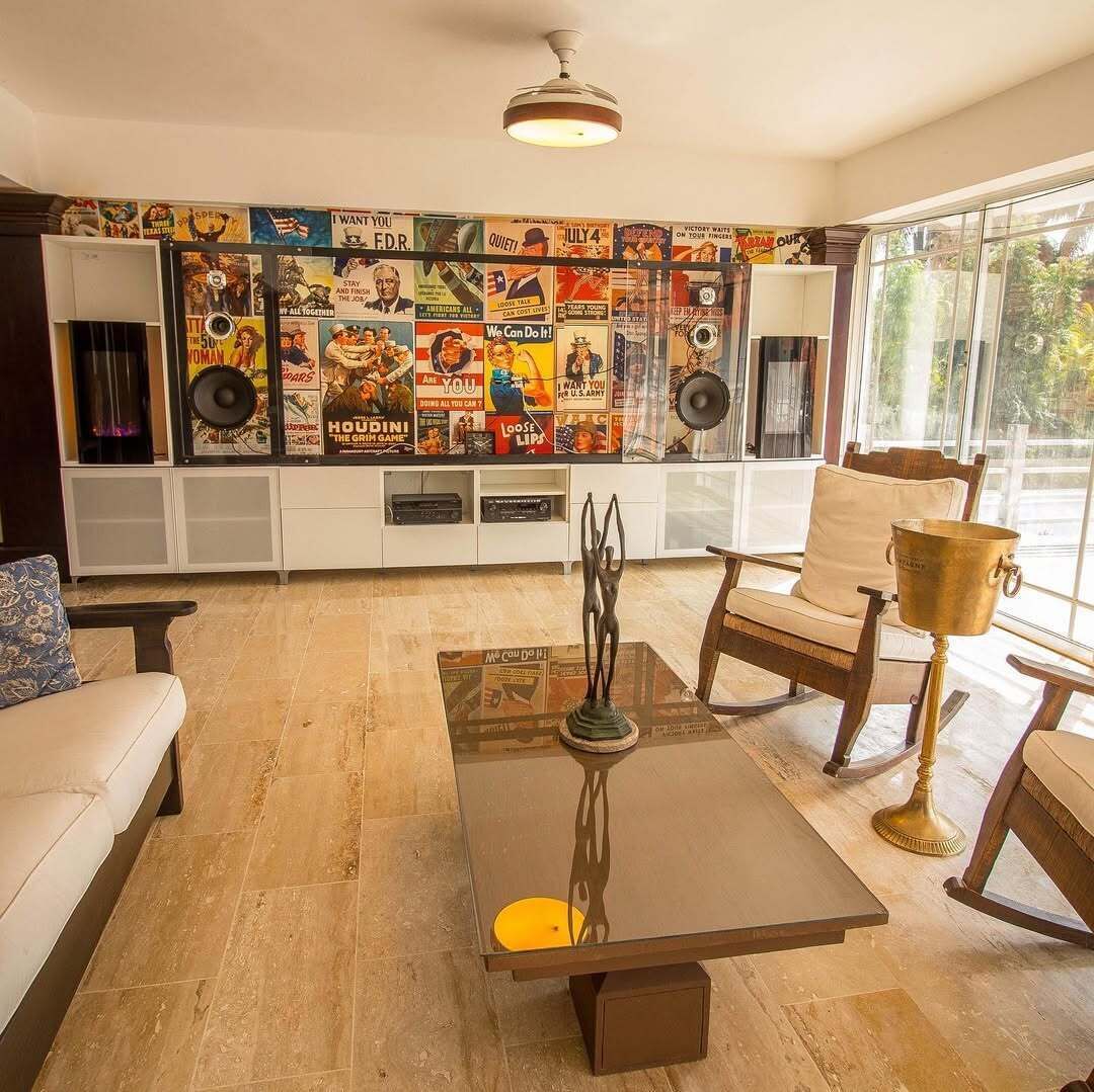 A living room with a large wall of vintage posters, a glass coffee table, and a view of the outdoors.