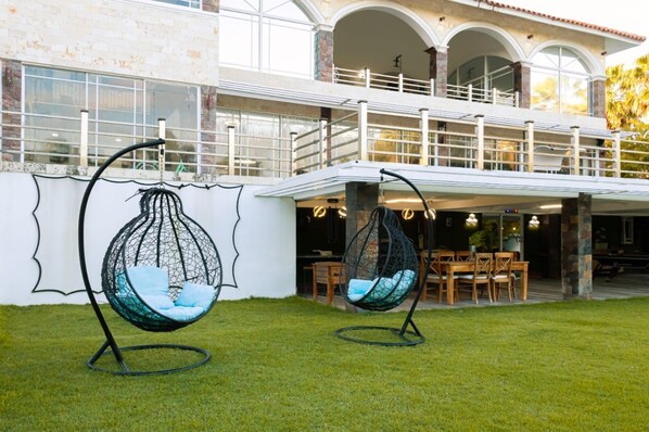 Una casa moderna con un amplio patio, dos sillas colgantes tipo huevo y una zona de comedor con mobiliario de madera.