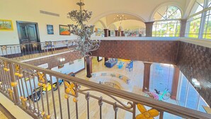Eine geräumige Lobby mit hoher Decke, einem Kronleuchter und Blick ins Freie durch große Fenster.
