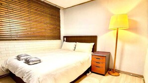 Een slaapkamer met een bed, nachtkastje, lamp en een raam met zonwering.