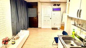 Een compacte keuken met een houten vloer, witte kastjes, een inbouwspoelbak en een klein eethoekje met een stoel.