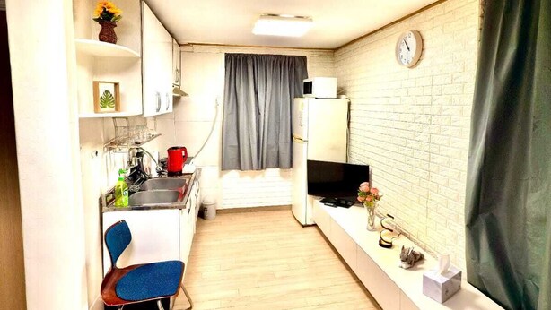 Een compacte keuken met een magnetron, spoelbak en een klein eethoekje met een stoel.