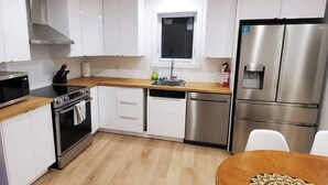 Une cuisine moderne avec des meubles blancs, des appareils en acier inoxydable, un plan de travail en bois et une fenêtre au-dessus de l’évier.