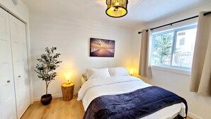 Une chambre à coucher avec un lit, des lampes de chevet, une plante en pot, un tableau et une fenêtre avec des rideaux.