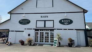 Een wit gebouw in de stijl van een schuur met borden voor 'Roxyann Winery Tasting Room' en 'Roxy Coffee'.