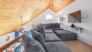 A modern loft bedroom with a sloped ceiling, a large window, a built-in sofa, and a flat-screen TV mounted on the wall.
