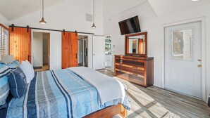 Ein Schlafzimmer mit Bett, Holzschrank, Deckenventilator, Fernseher und einer Tür mit Fenster.