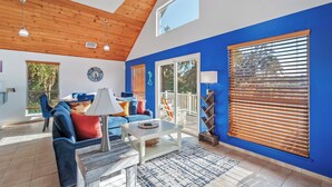 A spacious living area with a high ceiling, wooden beams, and a large window with blinds.