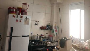 A kitchen with white tiled walls, a white refrigerator, a gas stove, and a window with blinds.