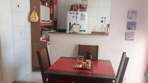 A compact kitchen with white tiles, a refrigerator, and a microwave. There is a dining table with chairs and a red rug.