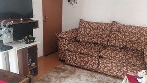 A living room with a sofa, a television, a wooden cabinet, and a small table with a toy.