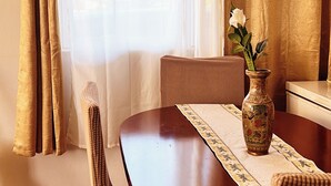 Een eetgedeelte met een houten tafel, twee stoelen, een vaas met bloemen en een raam met gordijnen.