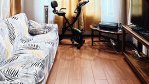 Een kamer met een bed, een hometrainer, een televisie en een plafondventilator.