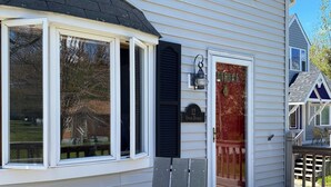 A wooden deck with a chair and a door to a house. - Charming Cottage in the Shadow of Day Mountain (Mount Desert)