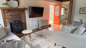 A living room with a fireplace, a television, and a sofa. - Charming Cottage in the Shadow of Day Mountain (Mount Desert)