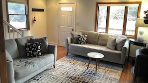 A living room with a grey sofa, a patterned rug, and a wooden coffee table. - Charming Cottage in the Shadow of Day Mountain (Mount Desert)