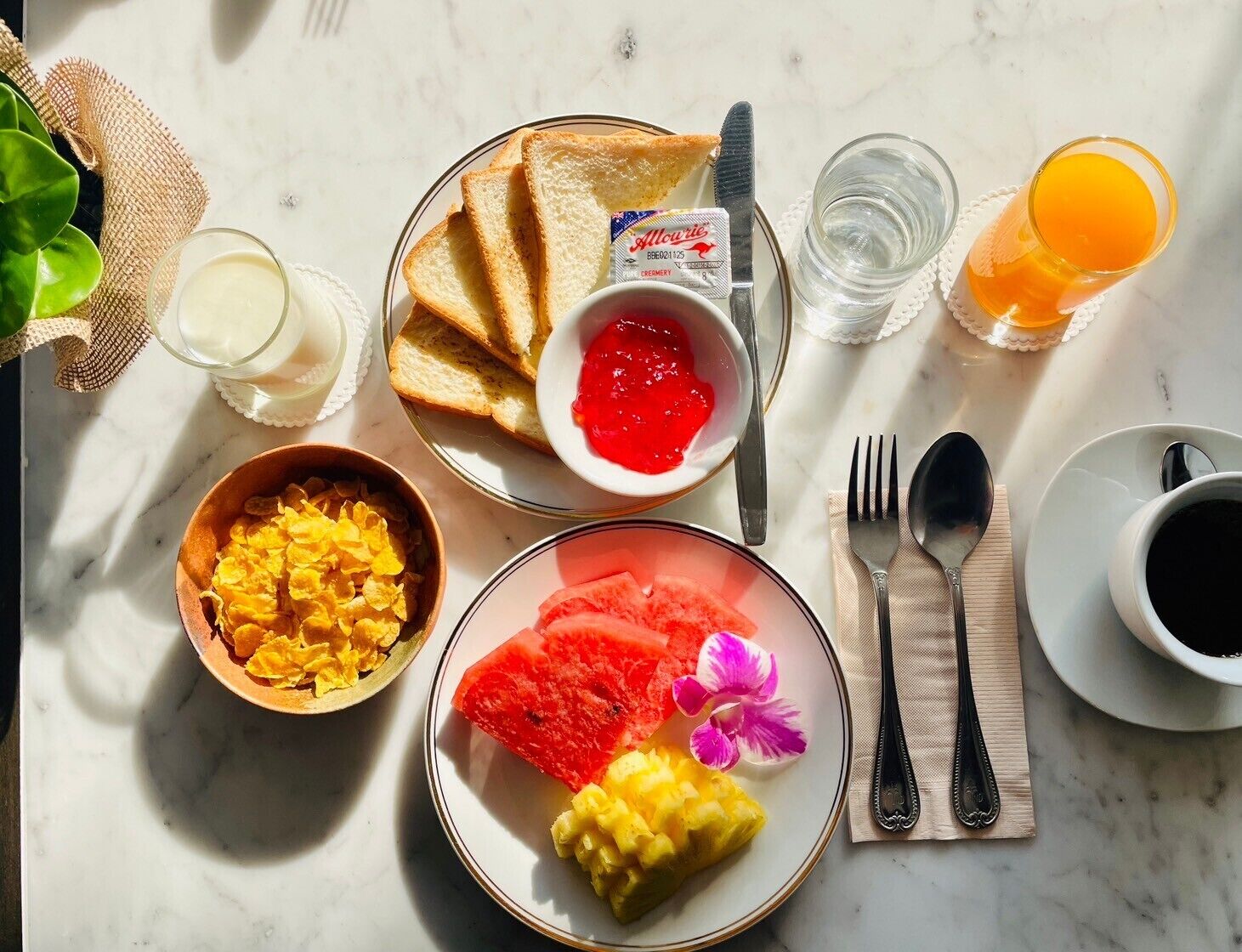 Desayuno con tostadas, mermelada, cereal, sandía, piña y un vaso de jugo de naranja.