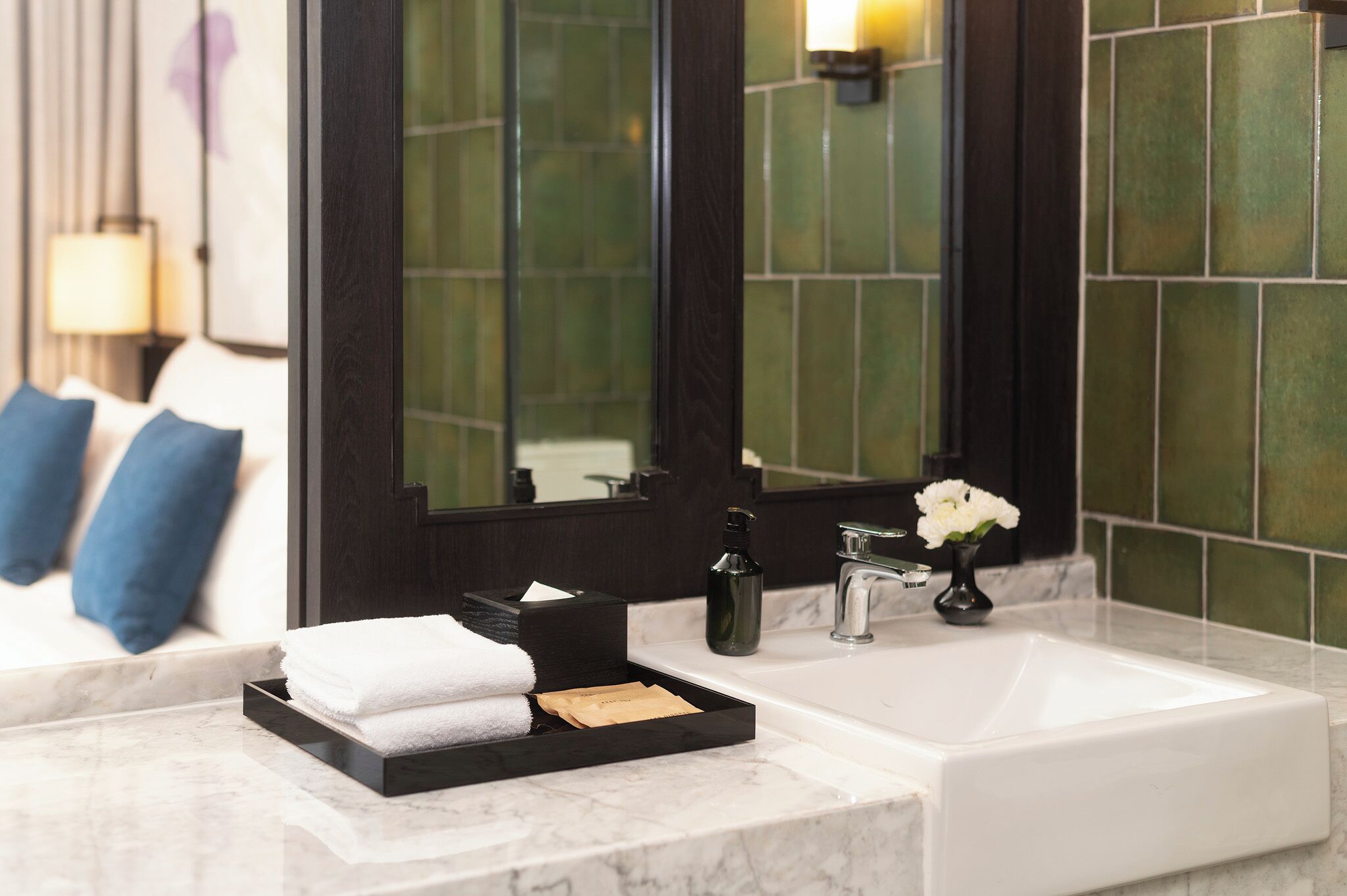 A bathroom with a white sink, a black tray with towels, a bottle, and a vase with flowers.