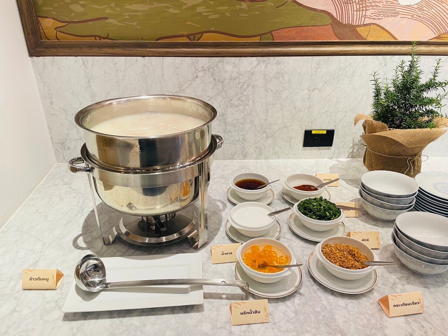 Una mesa de buffet con una olla grande de sopa, diferentes recipientes de condimentos y platos etiquetados.