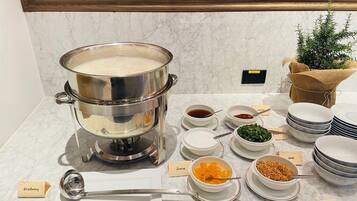 Una mesa de buffet con una olla grande de sopa, diferentes recipientes de condimentos y platos etiquetados.