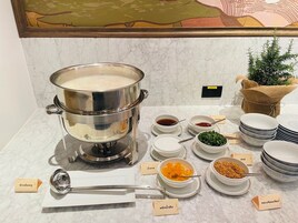 Una mesa de buffet con una olla grande de sopa, diferentes recipientes de condimentos y platos etiquetados.
