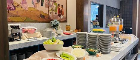A buffet setup with various food items and a juice dispenser.