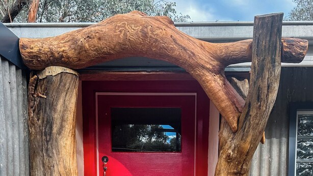 Una puerta roja con un arco de madera, un felpudo a cuadros blanco y negro, y un escalón que lleva a la puerta.