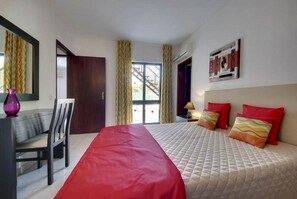 Une chambre d’hôtel avec un lit, un bureau, une chaise, une fenêtre avec des rideaux et un tableau au mur.