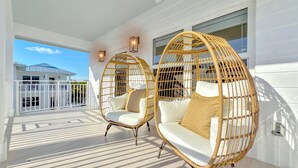 Two wicker chairs with white cushions on a balcony with a view of a house. - At The Sandbar: Partial Ocean View, Htd Pool, Free Dockage, GameRoom, EV Charger (Islamorada)