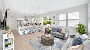 A modern kitchen with white cabinets, a stainless steel refrigerator, and a dining area with a round table and chairs. - At The Sandbar: Partial Ocean View, Htd Pool, Free Dockage, GameRoom, EV Charger (Islamorada)