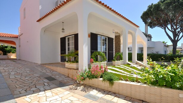 Un bâtiment blanc avec un toit recouvert de tuiles, un patio abrité et une entrée pavée de pierres.