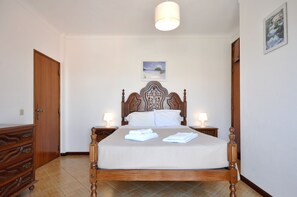 A bedroom with a wooden bed, two bedside tables with lamps, a wooden dresser, and a framed picture on the wall.