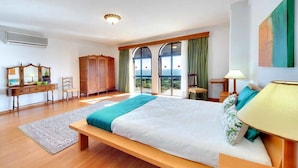 A spacious bedroom with a large bed, a wooden bench, a desk with a chair, and a view of the outdoors through large windows. - Relax by the pool at Villa Mar, minutes from Sao Rafael’s beaches (Sao Rafael)