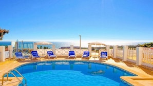 A swimming pool with blue lounge chairs and umbrellas, surrounded by a white fence, with a clear view of the sea in the background. - Relax by the pool at Villa Mar, minutes from Sao Rafael’s beaches (Sao Rafael)