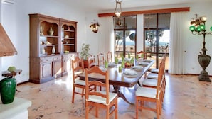 A dining area with a marble floor, wooden chairs, a long table set for a meal, and a large cabinet with shelves. - Relax by the pool at Villa Mar, minutes from Sao Rafael’s beaches (Sao Rafael)