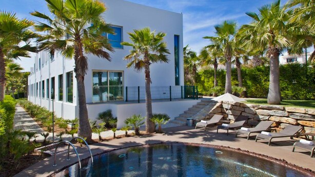 A modern building with a pool area, palm trees, and lounge chairs.