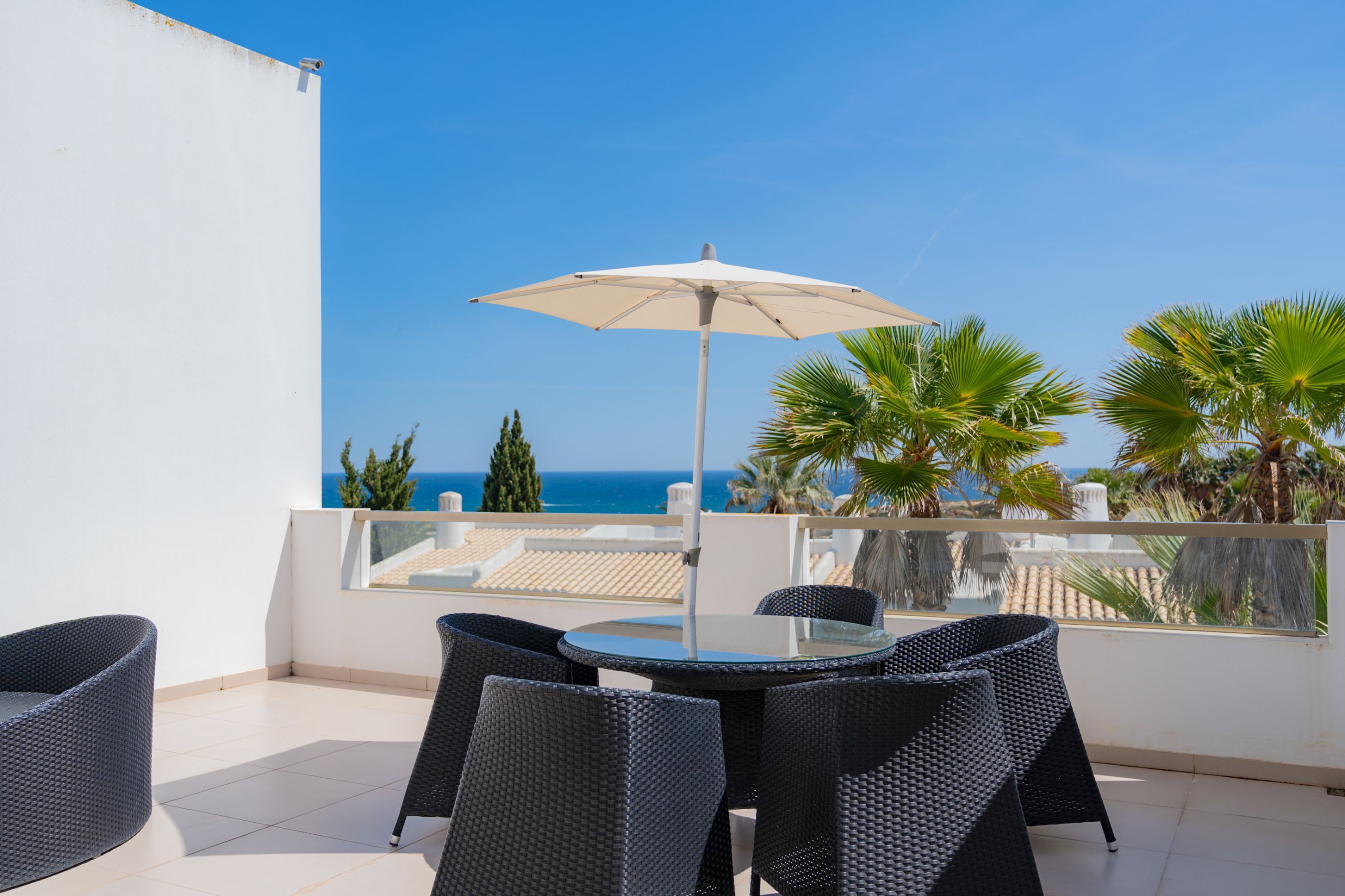 Een balkon met een ronde tafel en stoelen, een witte parasol en uitzicht op zee.