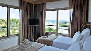 A hotel room with two beds, a TV, and a view of the sea.