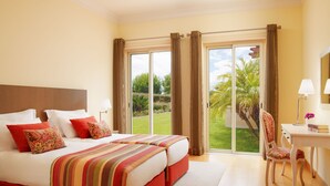 A hotel room with a large bed, a desk, and a view of a garden through the sliding doors.