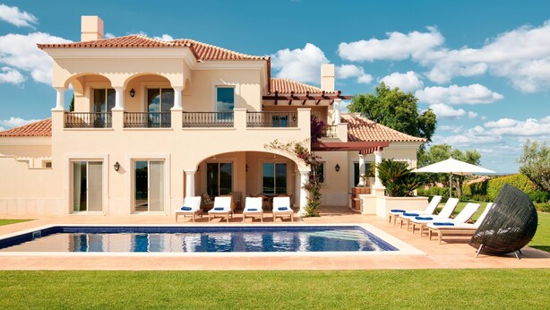 A two-story house with a swimming pool, outdoor seating, and a view of the ocean.