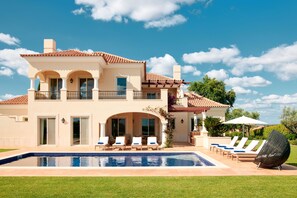 A two-story house with a swimming pool, outdoor seating, and a view of the ocean.