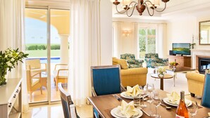 A well-lit, spacious living area with a dining table set for a meal, a sofa, and a television in the background.
