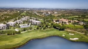 An aerial view of a golf course with a lake, surrounded by residential buildings and greenery.