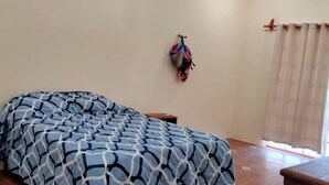 A bedroom with a bed, a nightstand, a wall-mounted air conditioner, a colorful bag, and a window with curtains. - Casa La Paz  (Merida)