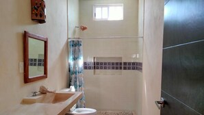 A bathroom with a sink, mirror, shower, and a small window. - Casa La Paz  (Merida)