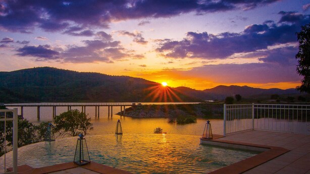 Una piscina con vistas a la puesta de sol, un puente y una cadena montañosa distante.