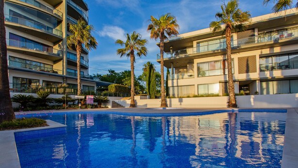 Piscina rodeada de palmeras y edificios modernos con balcones.