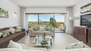 Una sala de estar moderna con sofá, mesa de centro y televisor. Hay un balcón con vistas al campo.