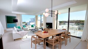 Ein geräumiges Wohnzimmer mit einem Holzessttisch, weißen Sofas und einem großen Fenster mit Blick auf die Stadt.
